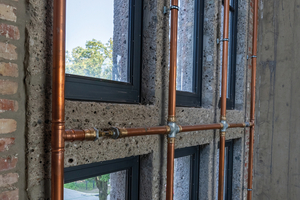  Die Kupferrohre entlang der großen Fenster im Altbau des Bergson Kunstkraftwerks sind Teil einer innovativen Lösung, um den denkmalgeschützten Naturstein vor Kondenswasser zu schützen. Sie erwärmen die Fassadenbereiche dezent und verhindern so Feuchtigkeitsschäden bei Veranstaltungen. Diese Technik verbindet historische Ästhetik mit moderner Funktionalität. 